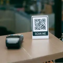 Stolik z terminalem płatniczym i tabliczką "SCAN ME" pokazuje, jak sie skanuje kod QR.