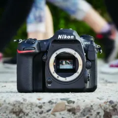 Nikon D500 na kamieniu, w tle nogi ludzi. Chcesz wiedzieć, jak sprawdzić przebieg aparatu?