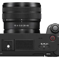 Czarny aparat Sony ZV-E1 z obiektywem FE 4-5.6/28-60. Widok z góry, z uchwytem na pasek i przyciskami sterującymi.