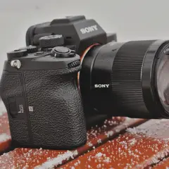 Aparat Sony a7s z obiektywem na ławce pokrytej śniegiem.