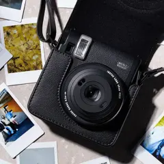Czarny aparat Instax w skórzanym etui, otoczony kilkoma natychmiastowymi zdjęciami. To właśnie instax co to za magia tworzenia wspomnień.