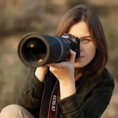 Kobieta z aparatem Canon EOS R7 w rękach, skupiona na kadrze. Pokazuje, jak ustawić aparat do idealnego ujęcia.
