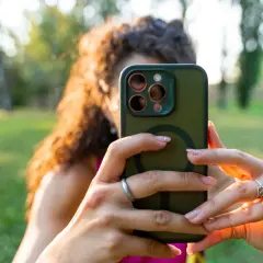 Kobieta z kręconymi włosami robi selfie zielonym smartfonem fotograficznym w parku.