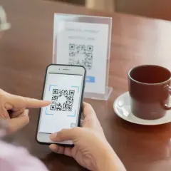 Osoba skanuje kod QR telefonem, by zapłacić bezgotówkowo. To prosty sposób, jak ściągnąć kod QR na telefon.