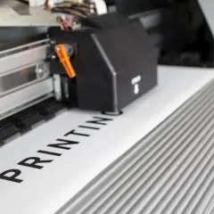 Drukarka wielkoformatowa drukuje napis "PRINTING". Dowiedz się, jak sprawdzić kolejkę drukowania.
