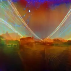 Widok na domy i pola, uchwycony w technice solarigrafii. Smugi światła tworzą surrealistyczny, tęczowy krajobraz.