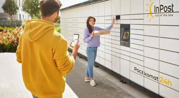 Mężczyzna z telefonem w ręku obserwuje kobietę, która wkłada paczkę do Paczkomatu InPost. Czy paczkomat InPost drukuje etykiety? Nie, ale ułatwia nadawanie.