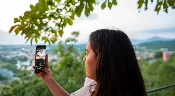 Kobieta robi zdjęcie telefonem. Aby uzyskać czysty kadr, pamiętaj, jak wyczyścić obiektyw w telefonie.