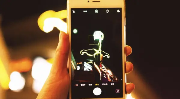 Dłoń trzyma smartfon, na ekranie którego widać interfejs aparatu. Można tu zobaczyć, jak zmienić aparat w telefonie, wybierając różne tryby fotografowania.