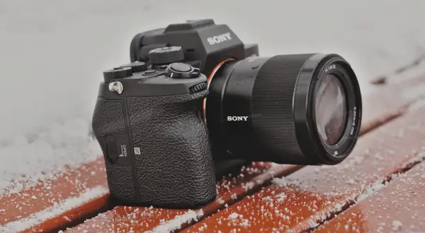 Aparat Sony a7s z obiektywem na ławce pokrytej śniegiem.