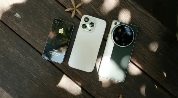 Trzy telefony do zdjęć: stary iPhone, nowy iPhone i smartfon z aparatem Leica, leżące na drewnianym stole.