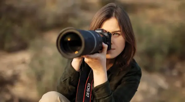 Kobieta z aparatem Canon EOS R7 w rękach, skupiona na kadrze. Pokazuje, jak ustawić aparat do idealnego ujęcia.