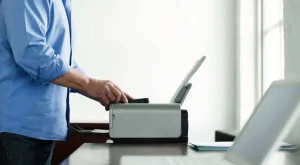 Mężczyzna w niebieskiej koszuli próbuje uruchomić drukarkę w trybie offline. Obok leży laptop.