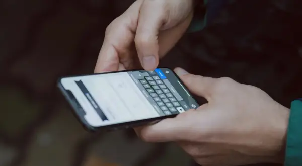 Dłonie trzymają smartfon z klawiaturą ekranową. Użytkownik wpisuje dane, być może szukając informacji, jak zainstalować drukarkę w telefonie.