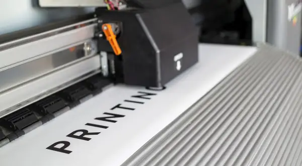 Drukarka wielkoformatowa drukuje napis "PRINTING". Dowiedz się, jak sprawdzić kolejkę drukowania.