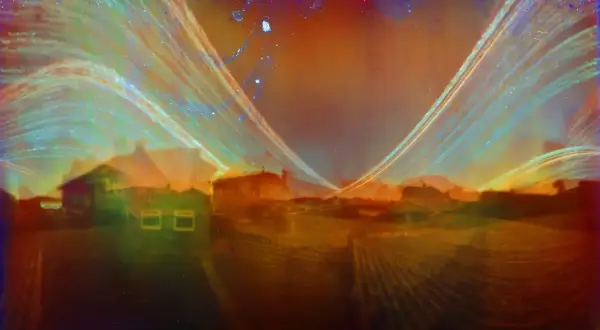 Widok na domy i pola, uchwycony w technice solarigrafii. Smugi światła tworzą surrealistyczny, tęczowy krajobraz.