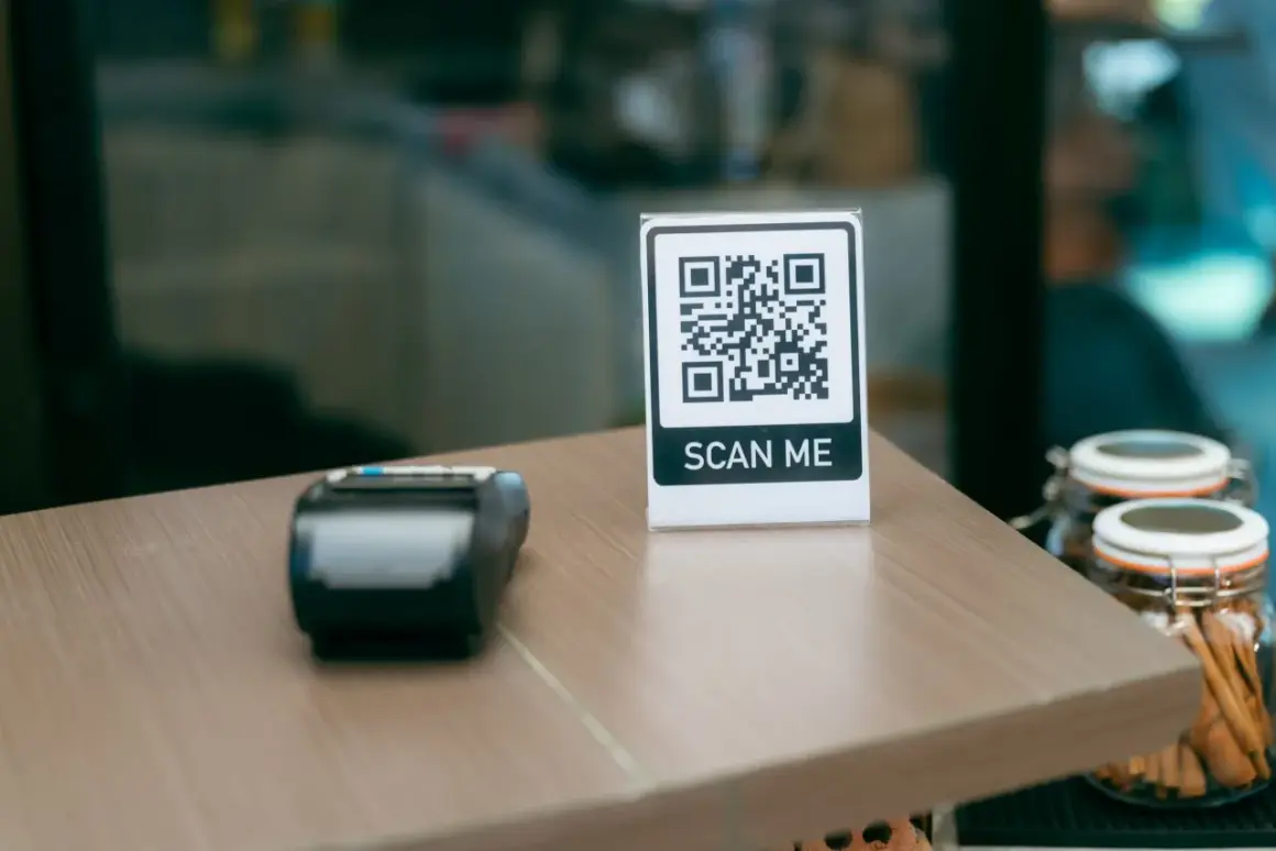 Stolik z terminalem płatniczym i tabliczką "SCAN ME" pokazuje, jak sie skanuje kod QR.