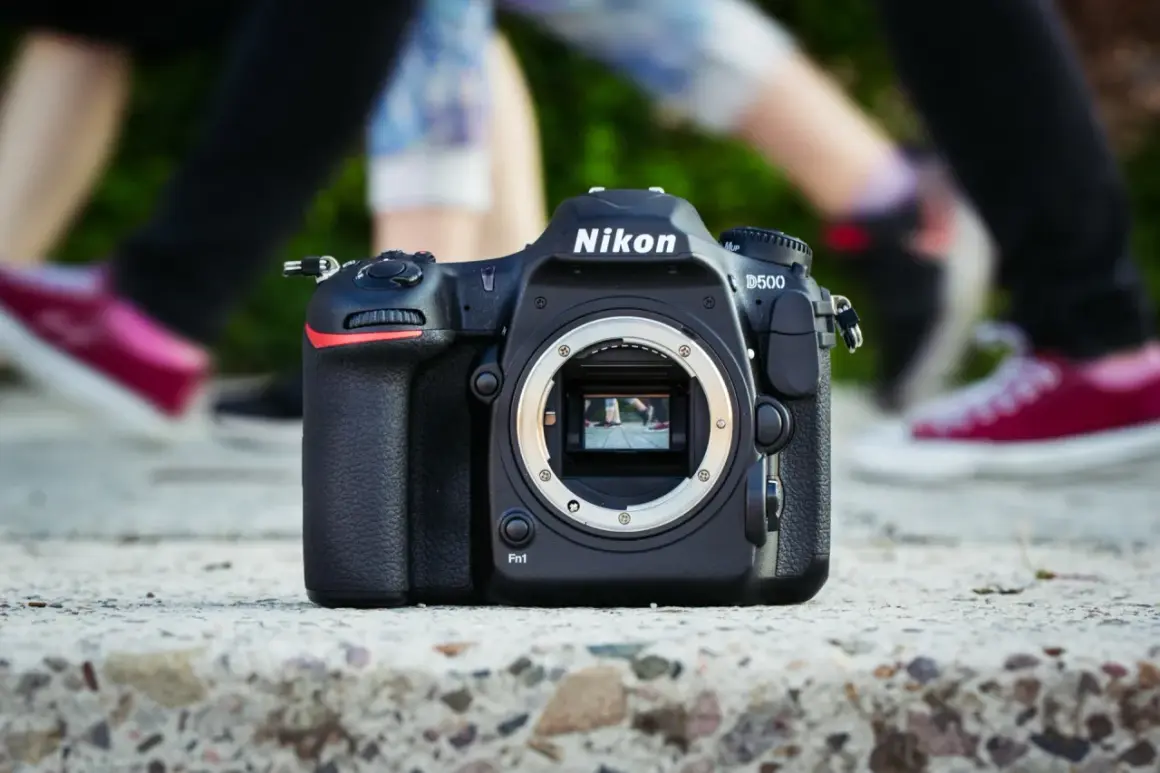 Nikon D500 na kamieniu, w tle nogi ludzi. Chcesz wiedzieć, jak sprawdzić przebieg aparatu?