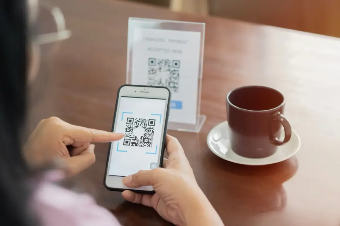 Osoba skanuje kod QR telefonem, by zapłacić bezgotówkowo. To prosty sposób, jak ściągnąć kod QR na telefon.